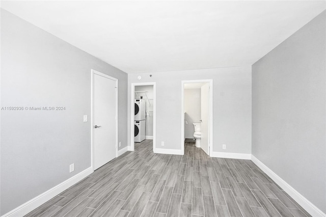 unfurnished bedroom featuring light hardwood / wood-style flooring, connected bathroom, and stacked washer and clothes dryer