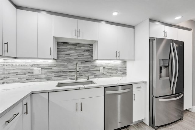 kitchen featuring sink, appliances with stainless steel finishes, tasteful backsplash, light stone counters, and white cabinetry