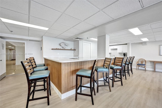 bar featuring a paneled ceiling, white cabinets, and light hardwood / wood-style floors