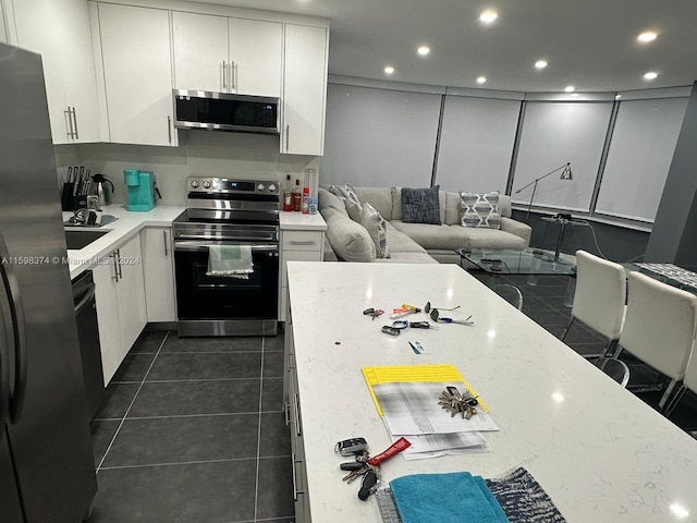 kitchen featuring white cabinetry, appliances with stainless steel finishes, light stone counters, sink, and dark tile flooring