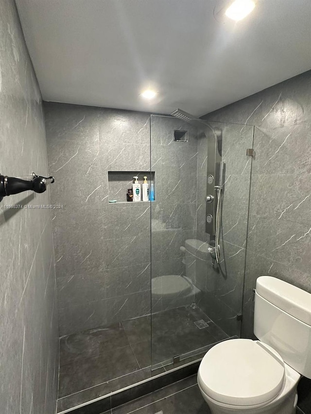 bathroom with tiled shower, toilet, and tile walls