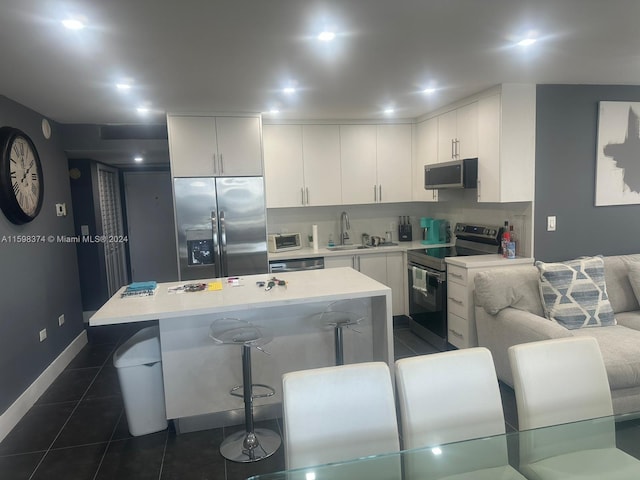 kitchen featuring appliances with stainless steel finishes, white cabinets, dark tile flooring, and a kitchen bar