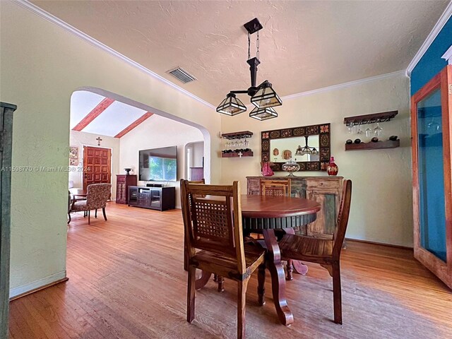 dining space featuring wood-type flooring, ornamental molding, a textured ceiling, and vaulted ceiling