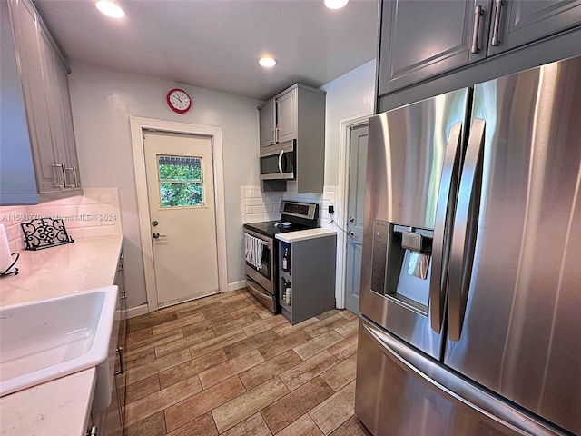 kitchen with stainless steel appliances, sink, decorative backsplash, and gray cabinetry