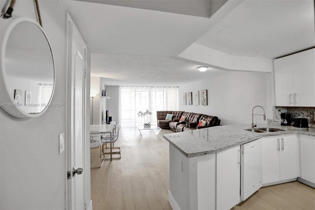 kitchen featuring kitchen peninsula, light stone countertops, light wood-type flooring, white cabinets, and sink