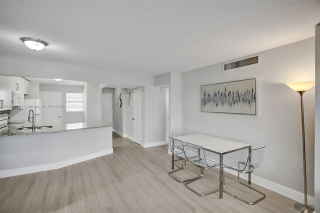 dining space with sink, a textured ceiling, and light wood-type flooring