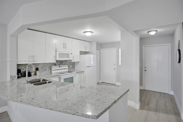 kitchen with light stone countertops, white appliances, white cabinetry, sink, and kitchen peninsula