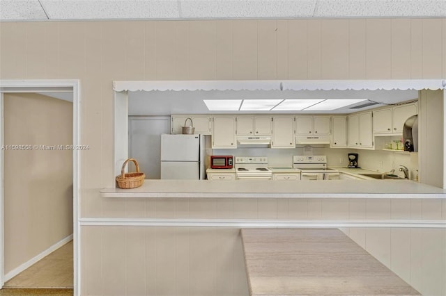 kitchen featuring sink, kitchen peninsula, cream cabinets, white appliances, and light tile patterned floors