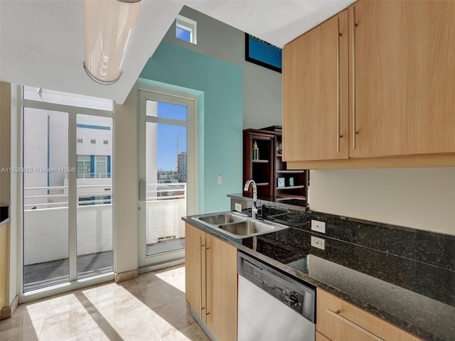 kitchen featuring dishwasher, sink, dark stone counters, light tile patterned floors, and light brown cabinets