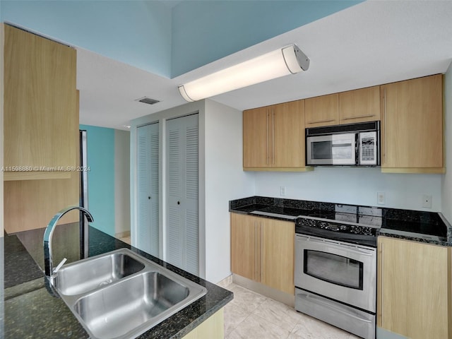 kitchen with dark stone countertops, sink, light tile patterned floors, and appliances with stainless steel finishes