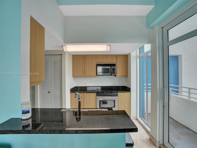 kitchen with expansive windows, appliances with stainless steel finishes, kitchen peninsula, and dark stone counters