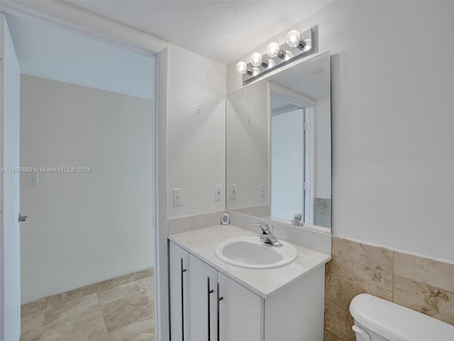 bathroom featuring vanity, tile walls, a textured ceiling, and toilet