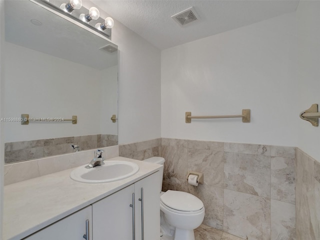 bathroom with toilet, a textured ceiling, tile walls, vanity, and tile patterned flooring