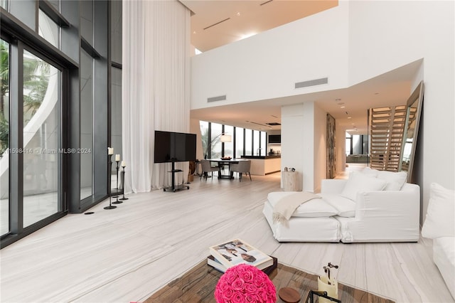 living room with a towering ceiling, a healthy amount of sunlight, and light wood-type flooring