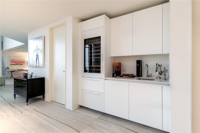 kitchen with wine cooler, white cabinetry, sink, and light hardwood / wood-style flooring