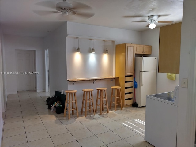 kitchen with a breakfast bar, light brown cabinets, light tile patterned floors, white fridge, and hanging light fixtures