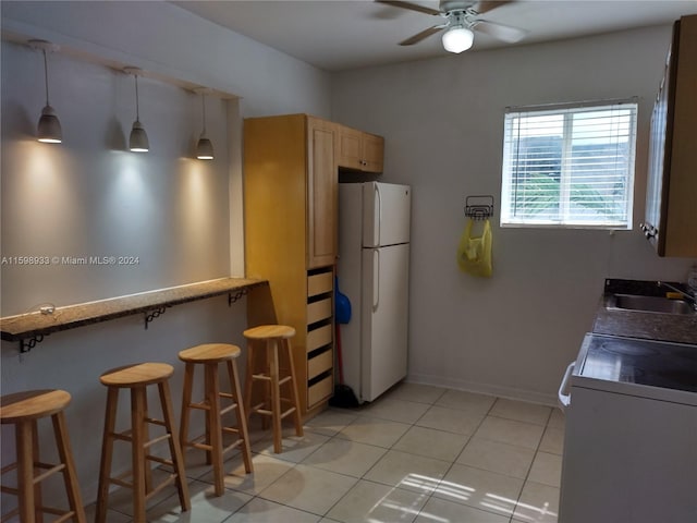 kitchen featuring a kitchen breakfast bar, white refrigerator, sink, light tile patterned floors, and decorative light fixtures