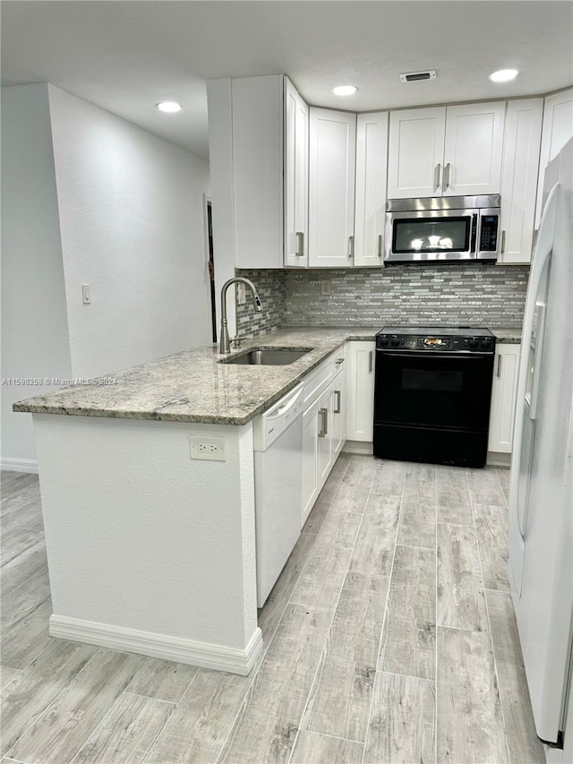 kitchen featuring white appliances, white cabinets, sink, kitchen peninsula, and light stone countertops