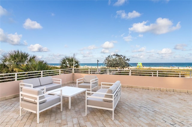view of patio / terrace featuring a water view, outdoor lounge area, fence, and a view of the beach