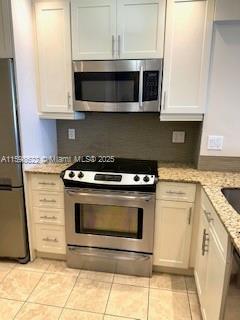 kitchen featuring light tile patterned floors, light stone countertops, stainless steel appliances, and decorative backsplash