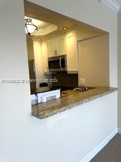 kitchen with white cabinetry, kitchen peninsula, a raised ceiling, and light stone countertops