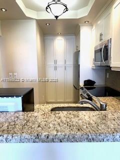 kitchen with a tray ceiling, white cabinetry, light stone counters, and stainless steel appliances
