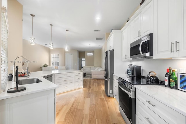 kitchen featuring appliances with stainless steel finishes, hanging light fixtures, light hardwood / wood-style floors, light stone countertops, and white cabinetry