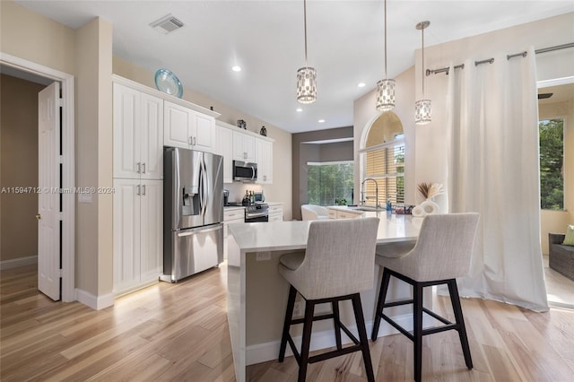 kitchen with light hardwood / wood-style floors, white cabinetry, hanging light fixtures, and stainless steel appliances