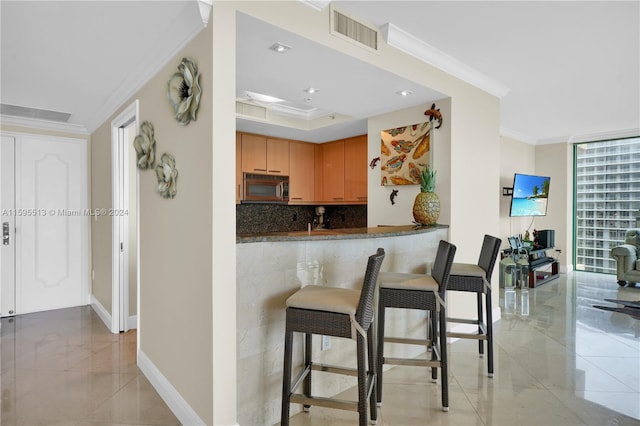 kitchen featuring kitchen peninsula, crown molding, dark stone countertops, a breakfast bar area, and decorative backsplash