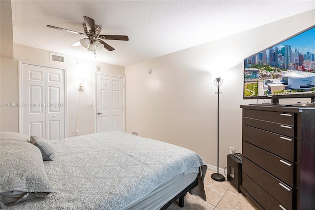 bedroom featuring ceiling fan, a closet, a textured ceiling, and light tile floors