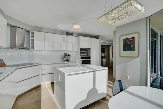 kitchen featuring wall chimney range hood, white cabinets, pendant lighting, and a kitchen island