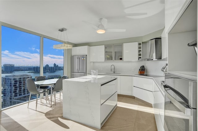 kitchen with pendant lighting, appliances with stainless steel finishes, white cabinetry, ceiling fan, and wall chimney range hood