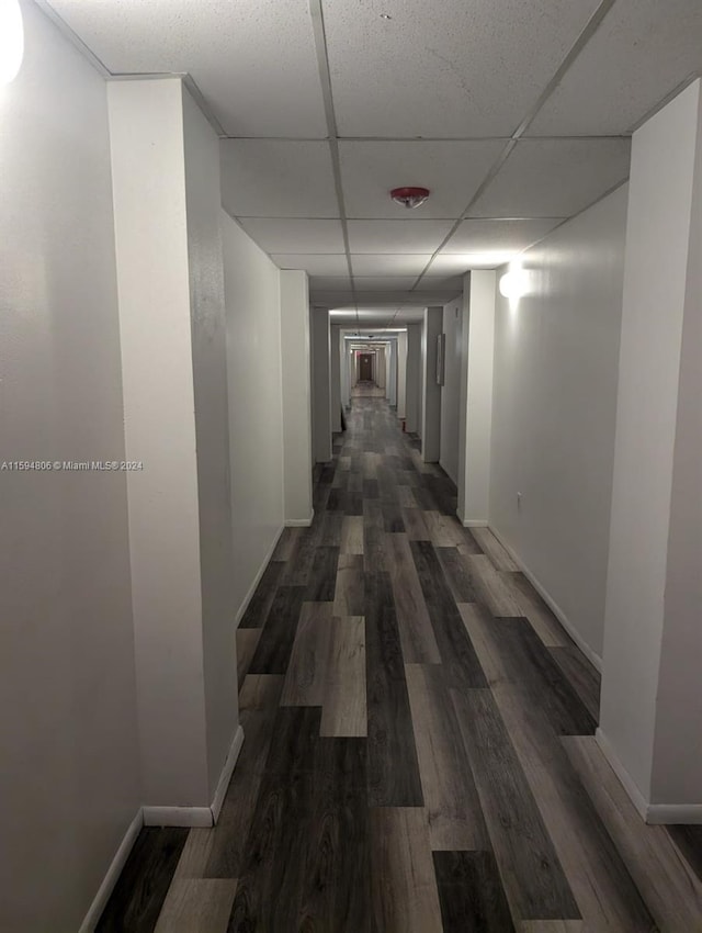 hall featuring a paneled ceiling, dark wood finished floors, and baseboards