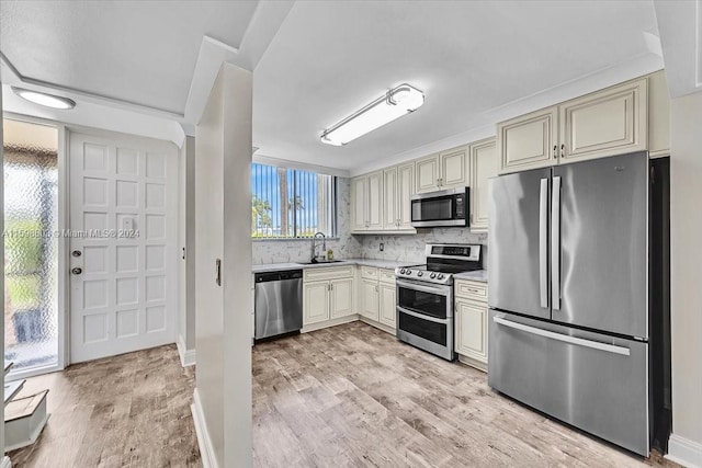 kitchen featuring sink, decorative backsplash, light wood-type flooring, cream cabinetry, and stainless steel appliances