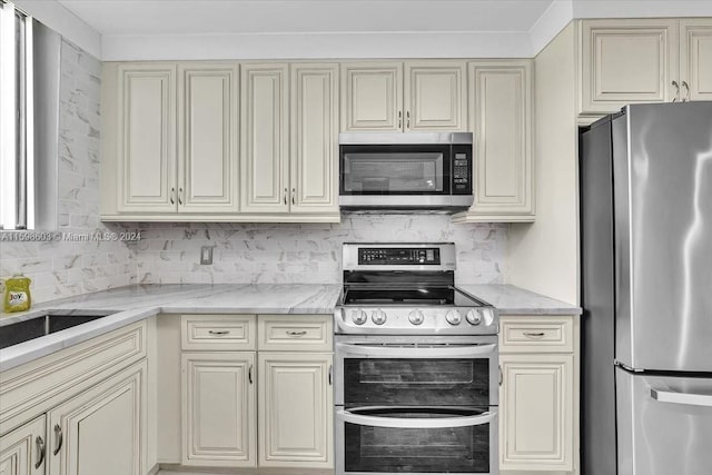 kitchen featuring cream cabinetry, appliances with stainless steel finishes, and light stone counters