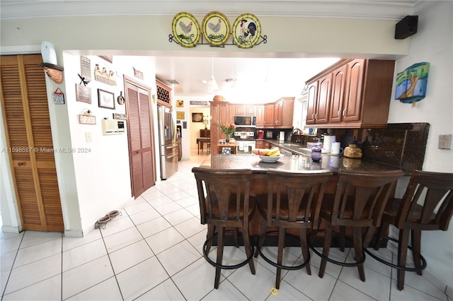 kitchen with sink, light tile patterned flooring, kitchen peninsula, a breakfast bar, and appliances with stainless steel finishes