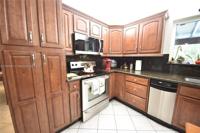 kitchen with stainless steel appliances, light tile patterned floors, backsplash, and dark stone counters