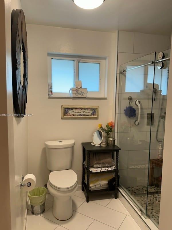 bathroom featuring toilet, tile patterned flooring, and a shower with shower door