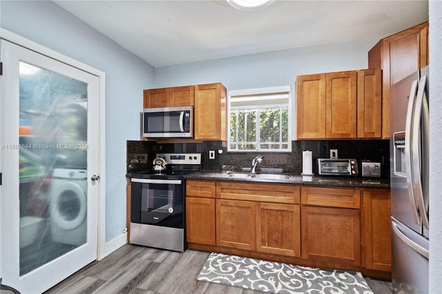 kitchen with light wood-type flooring, washer / dryer, tasteful backsplash, sink, and appliances with stainless steel finishes