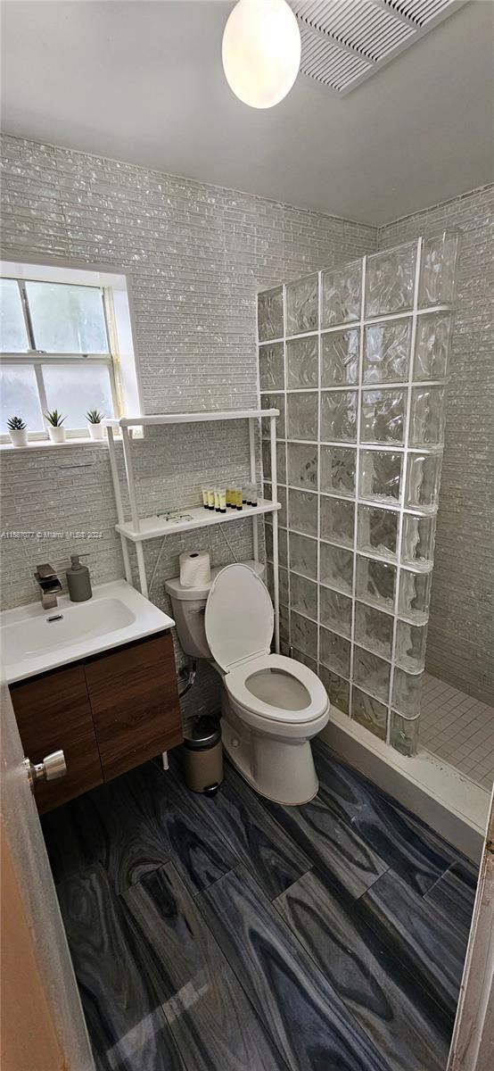 bathroom with a tile shower, tile walls, toilet, and vanity