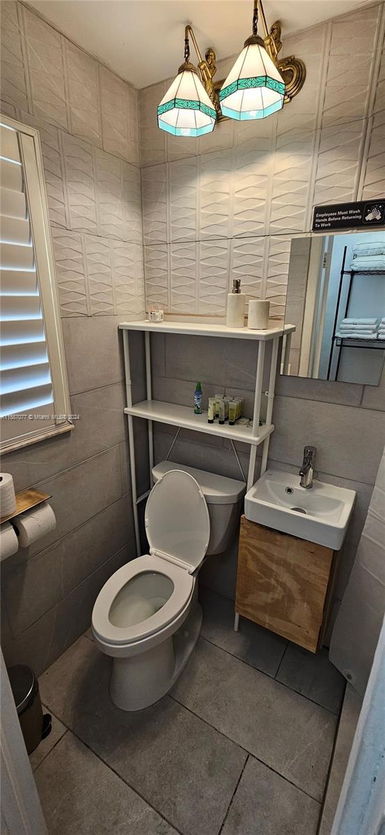 bathroom with vanity, toilet, tile floors, and tile walls