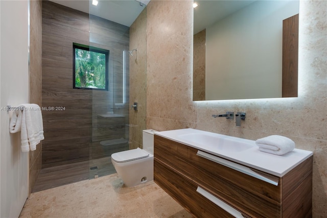 bathroom with a tile shower, vanity, tile walls, and toilet