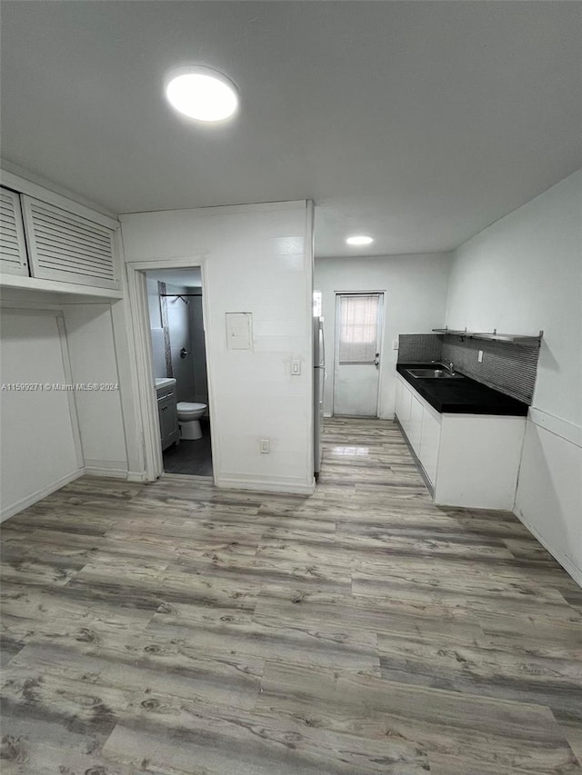 kitchen featuring white cabinetry, wood-type flooring, stainless steel refrigerator, and sink