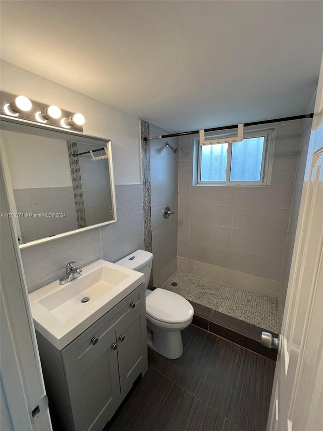 bathroom featuring tile patterned flooring, a tile shower, tile walls, toilet, and vanity