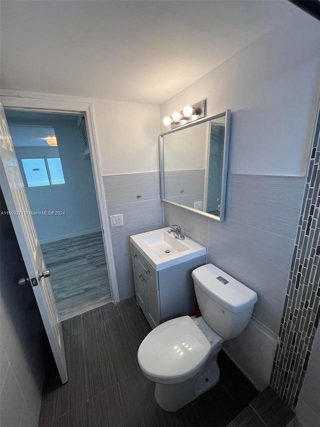 bathroom with toilet, vanity, tile patterned flooring, and tile walls