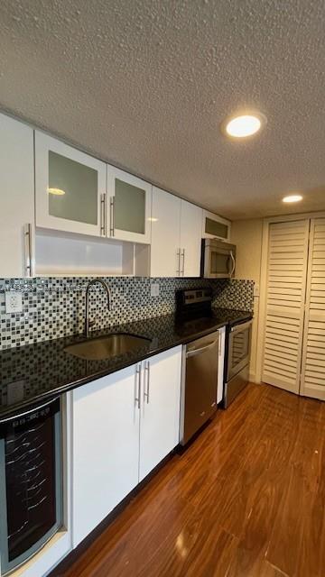 kitchen with tasteful backsplash, stainless steel appliances, sink, white cabinets, and wine cooler