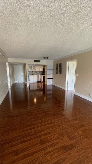 unfurnished living room featuring a textured ceiling, dark hardwood / wood-style flooring, and crown molding