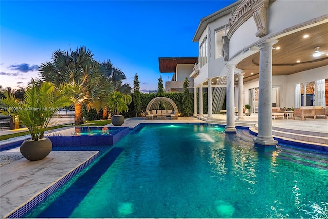 pool at dusk with a patio area and an in ground hot tub