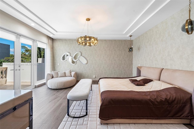 bedroom featuring hardwood / wood-style floors, a raised ceiling, access to exterior, and a chandelier