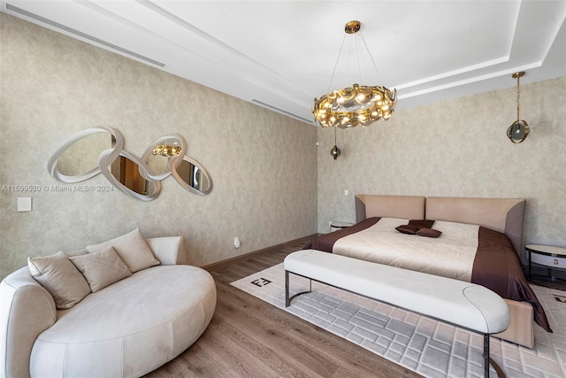 bedroom with a raised ceiling, wood-type flooring, and a chandelier